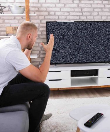 Segnale-TV-assente-uomo-seduto-divano-casa-alza-le-mani-disperato