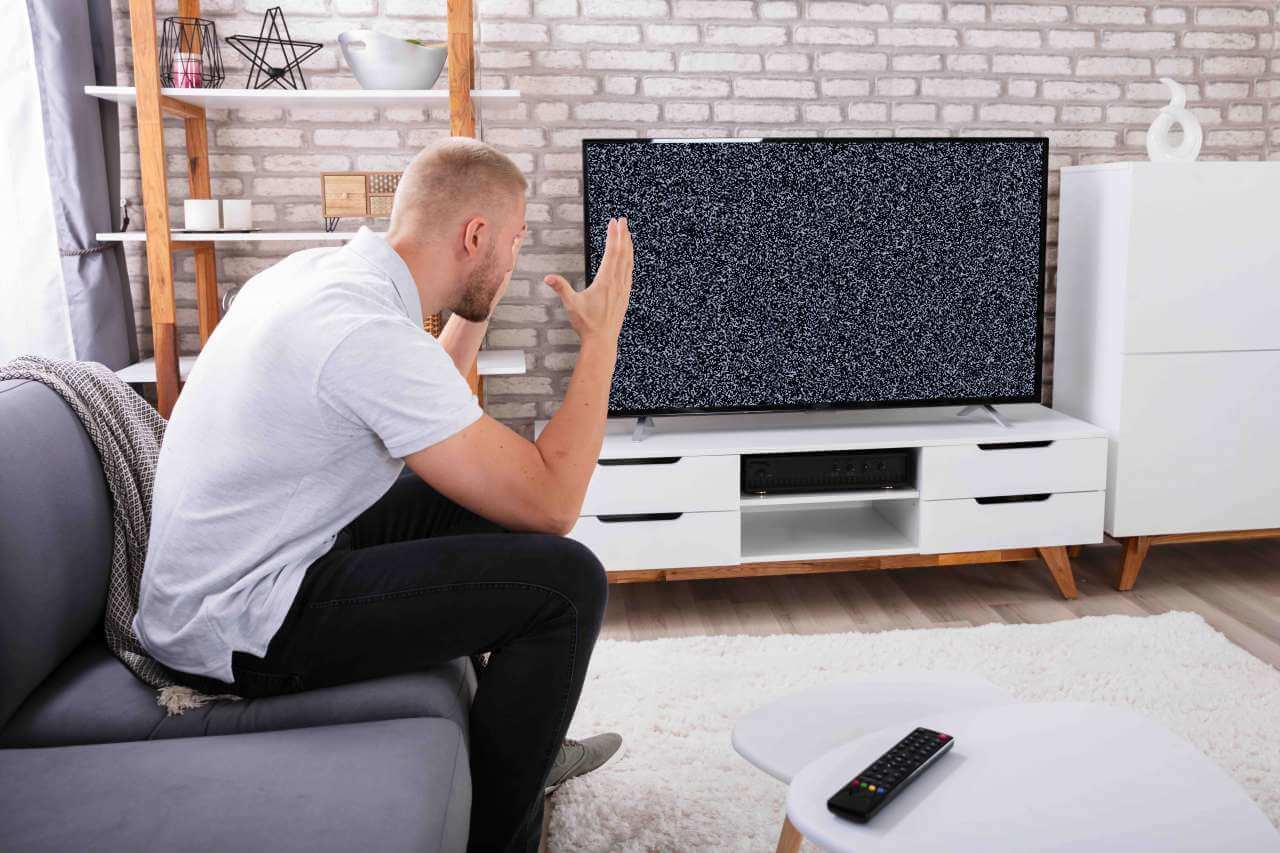 Segnale-TV-assente-uomo-seduto-divano-casa-alza-le-mani-disperato